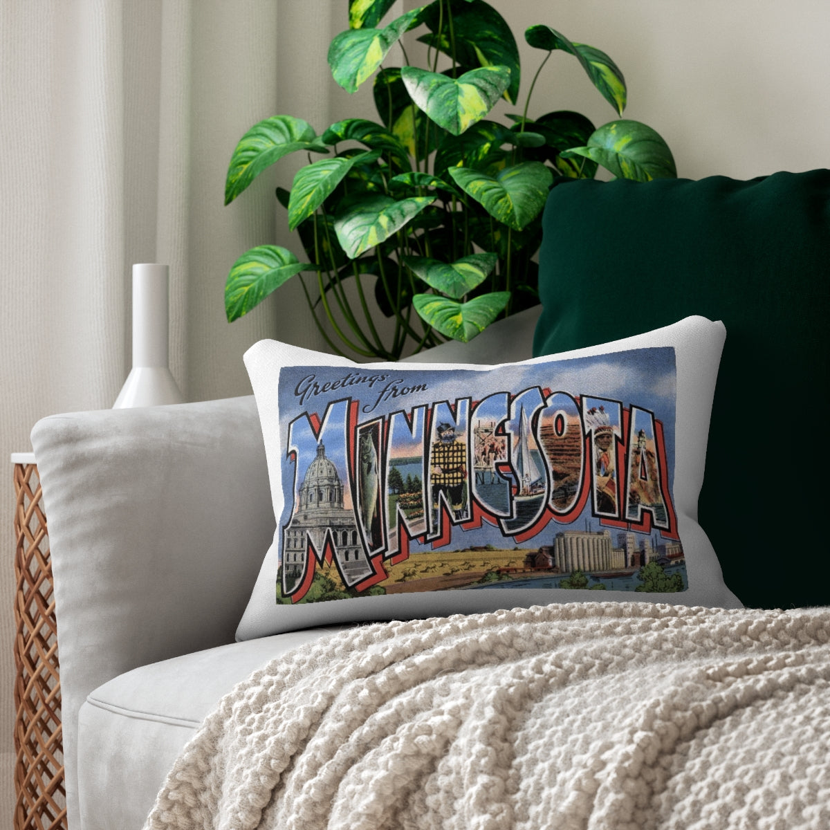 Minnesota lumbar pillow featuring a vintage Greetings from Minnesota postcard design on a light sofa beside a dark green cushion and cream knit blanket