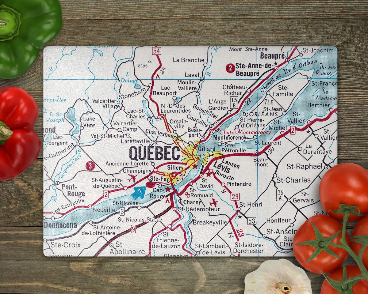 Quebec City vintage map glass cutting board featuring Levis and Ile d’Orleans with blue waterways and red roads on a wooden surface surrounded by vegetables